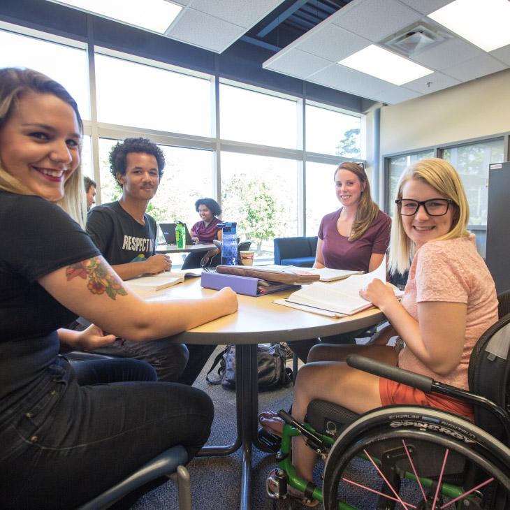 Four young adult students working at a table and smiling